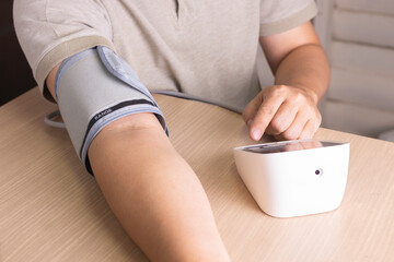 The man is checking blood pressure and heart rate with a digital pressure gauge by heself at home.