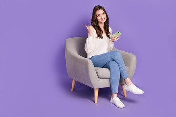 Obraz na płótnie Canvas Photo of positive satisfied lady sit chair hold modern device recommend quality gadgets empty space isolated on purple color background