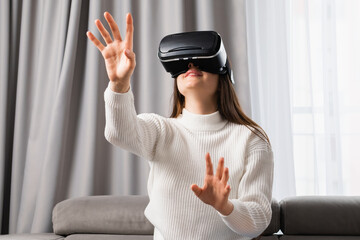 A beautiful caucasian woman uses VR headset touching an invisible screen sitting in the living...