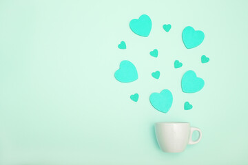 Coffee cup and blue wooden hearts on a mint color background. The concept of Valentine's day, love, dating and wedding. Symbol of a romantic gift or marriage proposal. Copy space, minimalism.