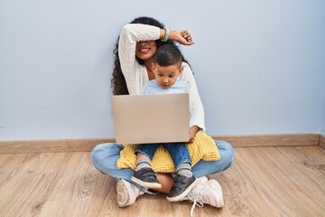 Young hispanic mother and kid using computer laptop sitting on the floor smiling cheerful playing...