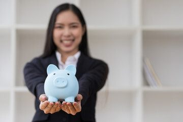 Obraz na płótnie Canvas Business woman holding a piggy bank inserting coins. Concept of savings.
