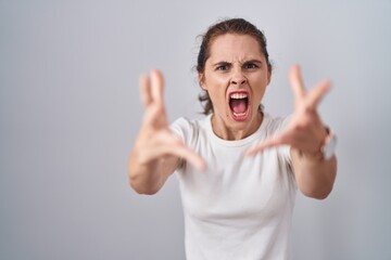 Beautiful brunette woman standing over isolated background angry and mad raising fists frustrated and furious while shouting with anger. rage and aggressive concept.