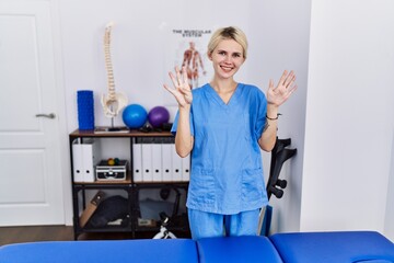 Young physiotherapist woman working at pain recovery clinic showing and pointing up with fingers...