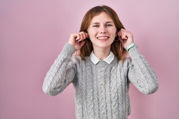 Beautiful woman standing over pink background smiling pulling ears with fingers, funny gesture....
