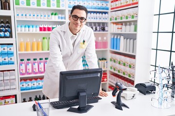 Young hispanic man pharmacist smiling confident using computer at pharmacy