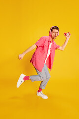 Fototapeta na wymiar Portrait of young man in bright clothes in headphones posing, dancing isolated over vivid yellow background
