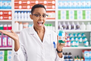 African american woman working at pharmacy drugstore holding syrup celebrating achievement with happy smile and winner expression with raised hand