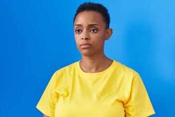 African american woman standing with serious expression over isolated blue background