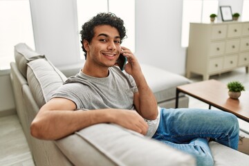 Young hispanic man talking on the smartphone sitting on the sofa at home.