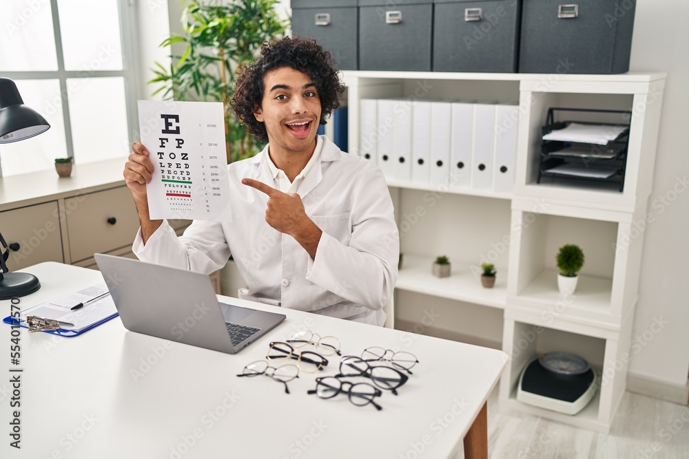 Wall mural hispanic man with curly hair holding eyesight medical exam smiling happy pointing with hand and fing