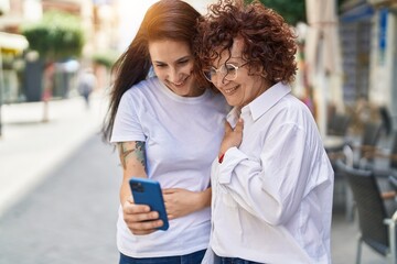 Two women mother and daughter standing together using smartphone at street