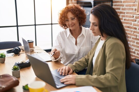Two women business workers using laptop speaking at office