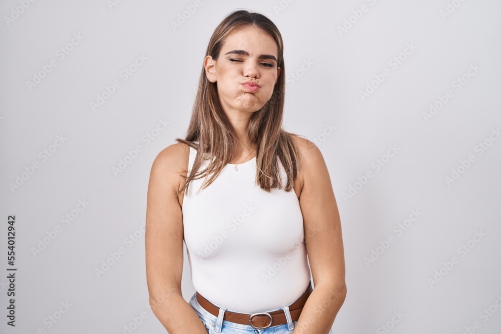 Sticker Hispanic young woman standing over white background puffing cheeks with funny face. mouth inflated with air, crazy expression.