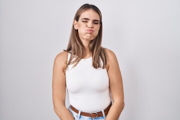 Hispanic young woman standing over white background puffing cheeks with funny face. mouth inflated...