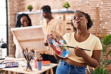 Young black painter woman at art studio holding palette looking at the camera blowing a kiss being lovely and sexy. love expression.