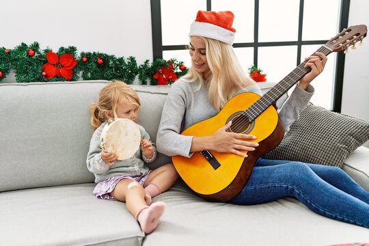 Mother and daughter playing guitar and tambourine sitting by christmas decor at home
