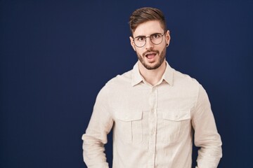 Hispanic man with beard standing over blue background afraid and shocked with surprise expression, fear and excited face.