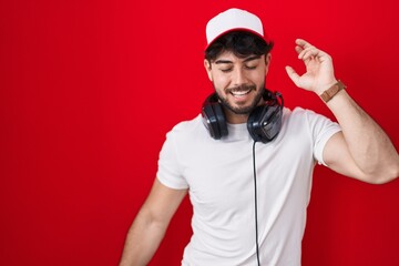 Fototapeta premium Hispanic man with beard wearing gamer hat and headphones dancing happy and cheerful, smiling moving casual and confident listening to music