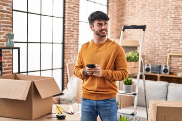 Young hispanic man smiling confident using smartphone at new home