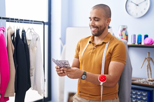 Young latin man tailor holding dollars at atelier