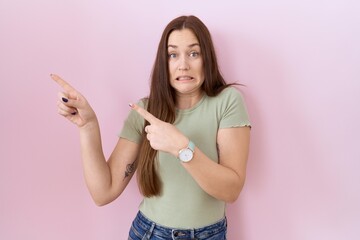 Fototapeta premium Beautiful brunette woman standing over pink background pointing aside worried and nervous with both hands, concerned and surprised expression