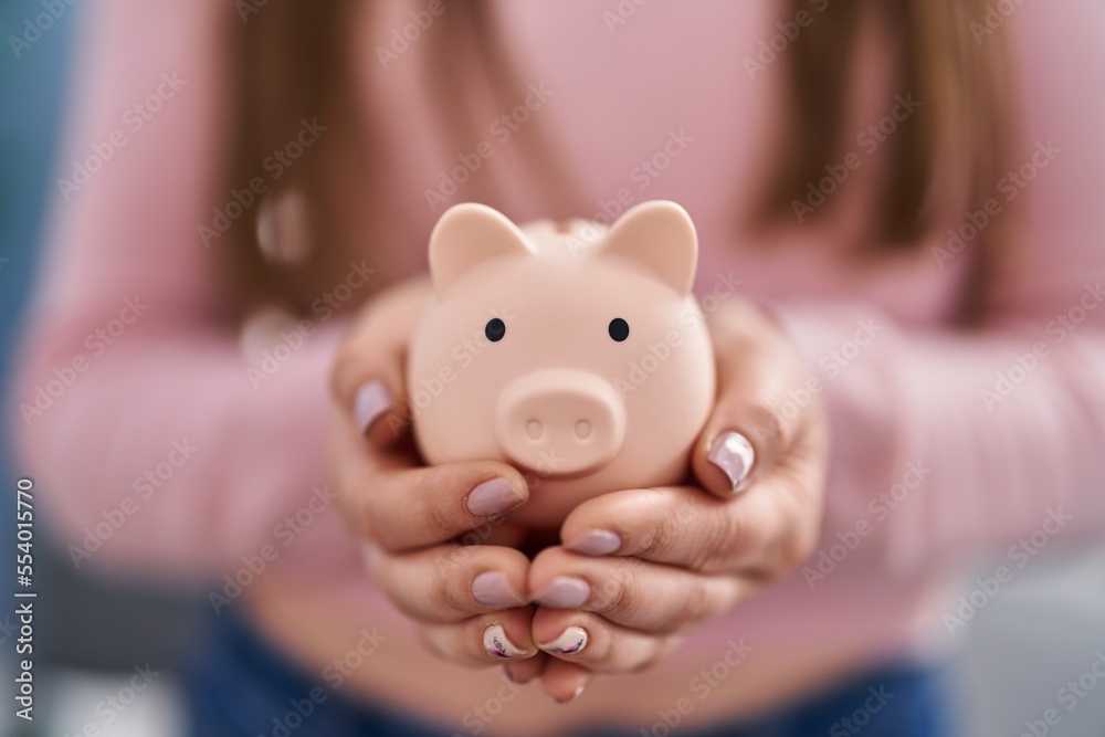 Wall mural young woman holding piggy bank at home