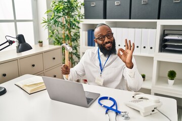 African american man working at medical clinic holding hammer doing ok sign with fingers, smiling friendly gesturing excellent symbol