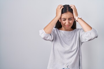 Young hispanic woman standing over white background suffering from headache desperate and stressed because pain and migraine. hands on head.