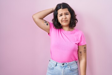 Young hispanic woman standing over pink background confuse and wondering about question. uncertain with doubt, thinking with hand on head. pensive concept.