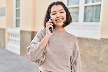 Young woman smiling confident talking on the smartphone at street
