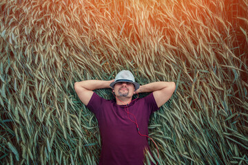 Worker in hat lying down on green wheat field and listening music with earphones. Lifestyle and freedom concept. © Bonsales