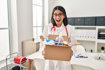 Young hispanic doctor woman holding box with medical items celebrating crazy and amazed for success with open eyes screaming excited.