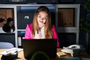 Obraz premium Young caucasian woman working at the office at night doing happy thumbs up gesture with hand. approving expression looking at the camera showing success.