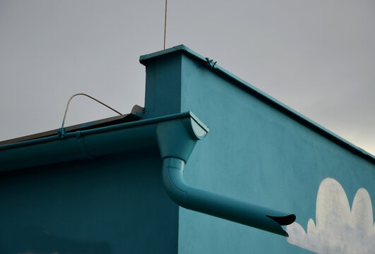 a building painted turquoise, including a gutter and a water spout. the kindergarten has a facade decorated with clouds