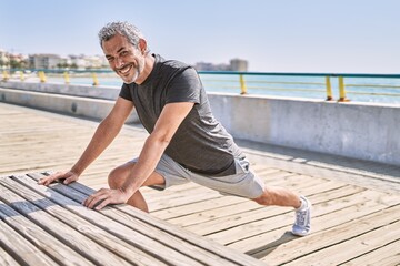 Fototapeta na wymiar Middle age hispanic man wearing sportswear stretching at seaside