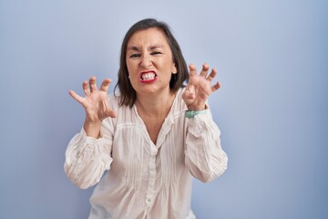 Middle age hispanic woman standing over blue background smiling funny doing claw gesture as cat,...