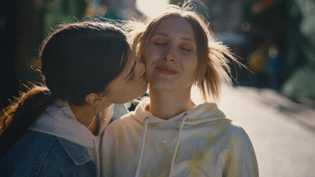 Lesbian couple together, standing downtown feeling in love. Partner kissing on a cheek her girlfriend and smile standing on the street. Pride, Lgbt relationships