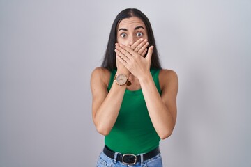 Young woman standing over isolated background shocked covering mouth with hands for mistake. secret...