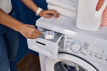 Young blonde woman pouring detergent on washing machine at laundry room