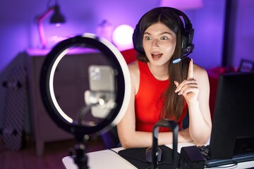 Young caucasian woman playing video games recording with smartphone surprised with an idea or question pointing finger with happy face, number one