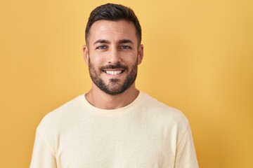 Handsome hispanic man standing over yellow background with a happy and cool smile on face. lucky...
