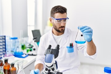 Young hispanic man wearing scientist uniform holding test tube at laboratory