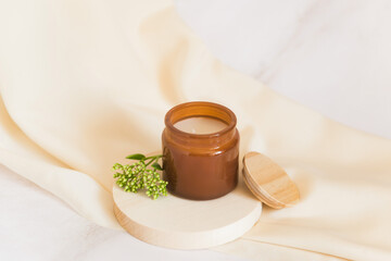 aroma candle on silk cloth background with green twigs and wooden podium