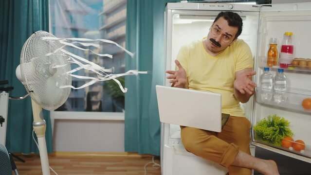 problem of hot weather , a disgruntled male freak with a mustache experiencing overheating cools down sitting in the refrigerator with a laptop