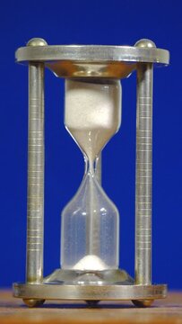 Vertical video social media format – Closeup isolated shot of a traditional vintage glass egg timer, encased in an elegant steel holder, with the trickling sand at the start of its flow.