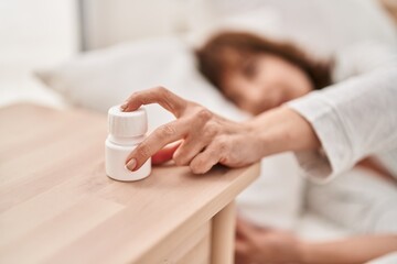 Middle age woman taking pills to sleep lying on bed at bedroom