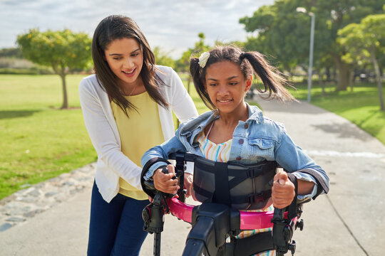 Mother helping disabled daughter walking in rollator at park