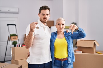 Hispanic mother and son holding keys of new home with angry face, negative sign showing dislike...