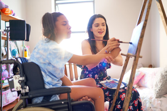 Mother and disabled daughter in pushchair painting in bedroom
